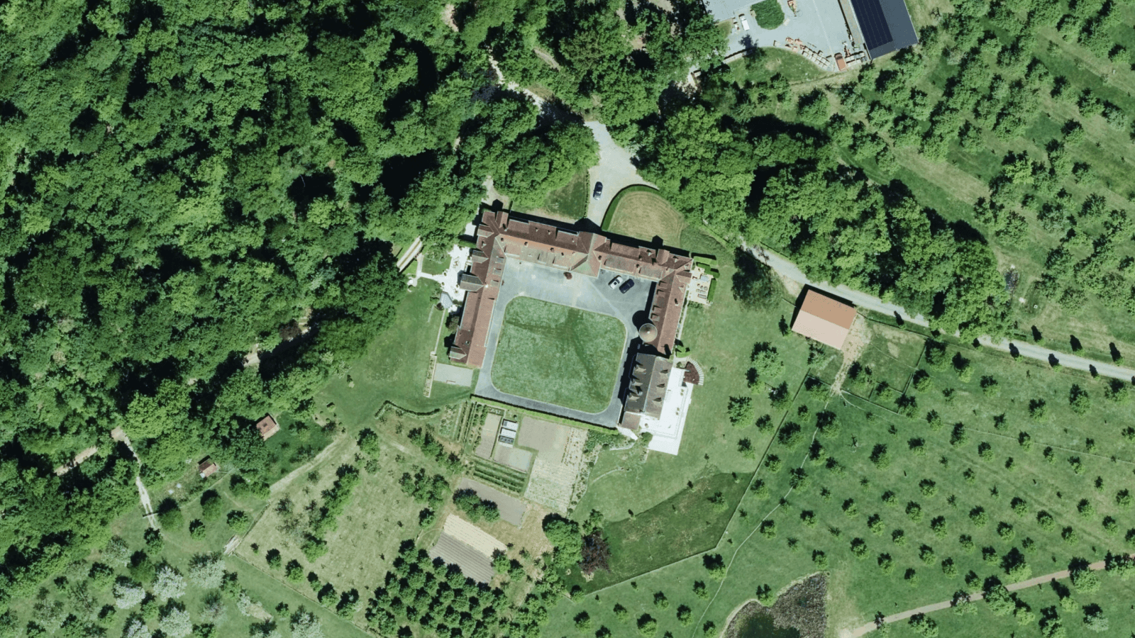Top-down aerial imagery showing a historic courtyard building surrounded by lush green forests and farmland in Luxembourg.